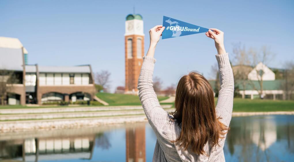 Student holds a #GVBound pennant up in front of carillon tower